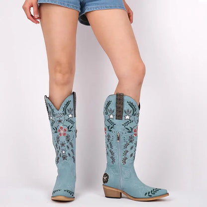 Light blue cowboy boots with floral patterns worn by a person on a white background