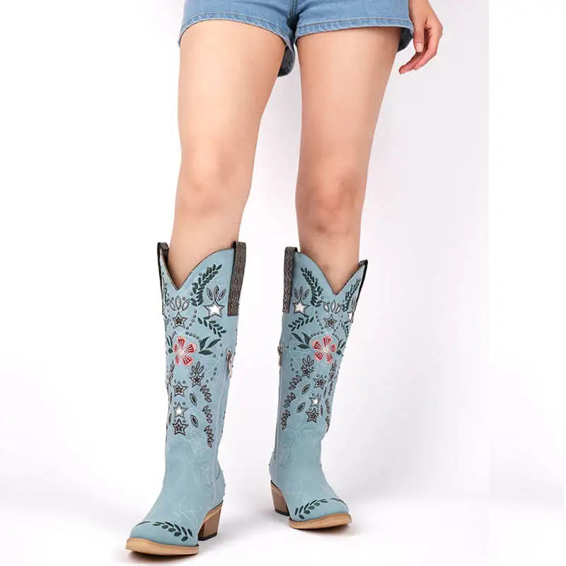 Light blue embroidered cowboy boots worn with denim shorts on a white background