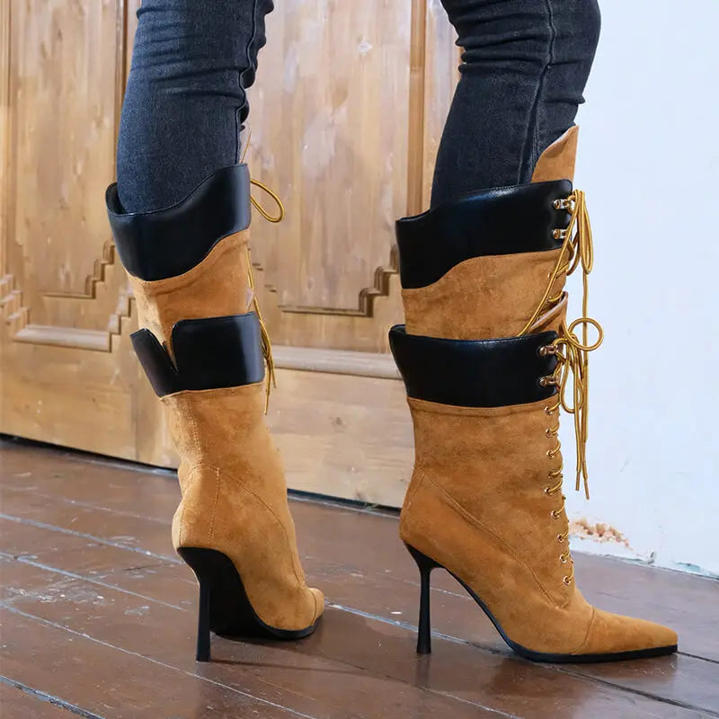 Tan knee-high boots with black accents worn by a person on a wooden floor.