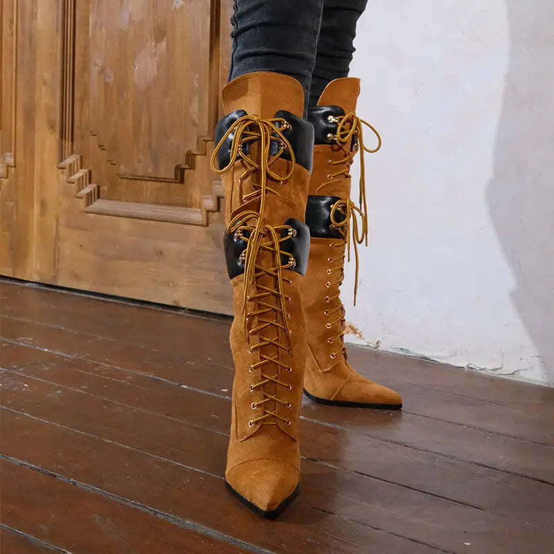 Brown suede knee-high boots with laces on a wooden floor.